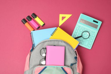 Sırt çantası ve pembe arka planda farklı okul malzemeleri.