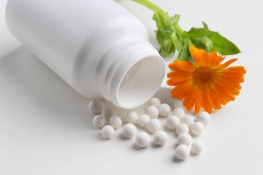 Homeopatik tedavi. Beyaz arka planda bir sürü hap ve çiçek olan şişe, yakın plan.
