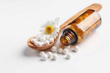 Homeopatik tedavi. Beyaz arka planda haplı kaşık, şişe ve papatya çiçeği.