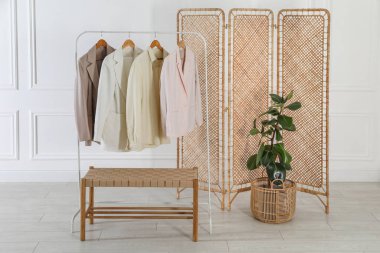 Katlama ekran, elbise askısı, depolama tezgahı ve beyaz duvarın yanındaki bitki örtüsü.