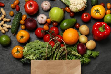 Vejetaryen yemek servisi. İçinde farklı taze sebzeler, fındıklar ve meyveler olan kağıt torba koyu dokulu masa, düz uzanmış.