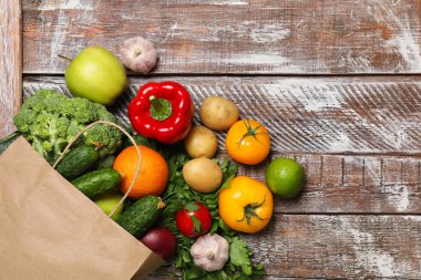Vejetaryen yemek servisi. Farklı taze sebzelerle dolu kağıt torba ve ahşap kırsal masada meyveler, düz yatak. Metin için boşluk