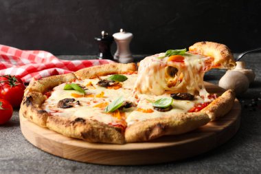 Gri masada lezzetli vejetaryen pizzasından bir parça alıyorum, yakın plan.