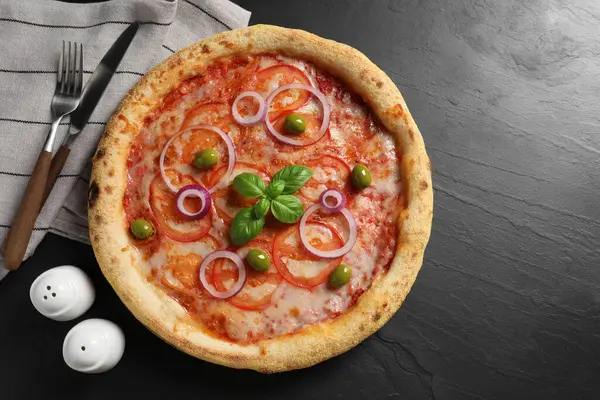 Lezzetli vejetaryen pizza, çatal bıçak takımı, siyah masada tuz ve biber, üst manzara.