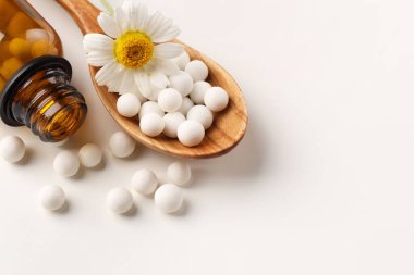Homeopatik tedavi. Beyaz arka planda haplı kaşık, şişe ve papatya çiçeği. Metin için boşluk