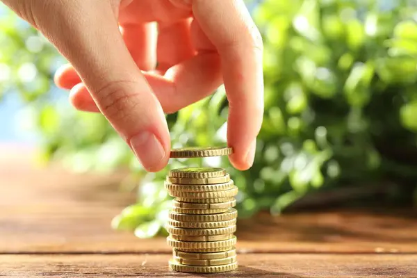 stock image Woman stacking coins at wooden table, closeup