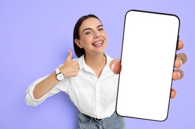 Mavi menekşe arka planında boş ekranlı cep telefonu gösteren mutlu bir kadın. Tasarım için model