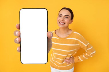 Portakal rengi arka planda boş ekranlı cep telefonu gösteren mutlu bir kadın. Tasarım için model