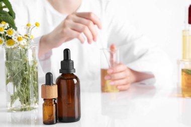 Aromaterapi ürünü. Laboratuvarda beyaz masada gerekli yağları üreten bilim adamı, şişelere odaklanıyor