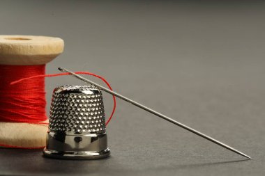 Kırmızı iplikli dikiş iğnesi, gri arka planda makara ve yüksük, yakın plan. Metin için boşluk