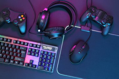 Bilgisayar faresi, RGB klavyesi, kulaklık ve oyun denetleyicileri koyu arkaplan üzerinde neon ışıklar, üst görünüm