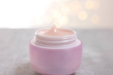 Gri masaya bir kavanoz krema. Arka planda bulanık ışıklar, yakın plan.