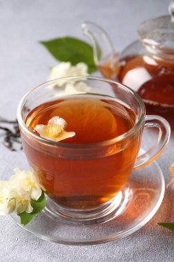 Sıcak yasemin çayı fincanda ve çiçekler açık gri masada.
