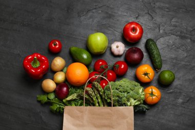 Vejetaryen yemek servisi. Farklı taze sebzelerle dolu kağıt poşet ve koyu dokulu masa üzerinde meyveler, düz uzanmış.