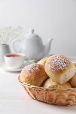 Sepette pudra şekerli lezzetli hamur topları, çay, çaydanlık ve beyaz ahşap masada çingene çiçekleri.