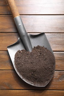 Tahta masanın üzerinde toprak olan metal kürek, üst manzara.