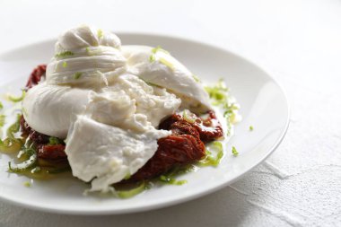 Lezzetli burrata peyniri ve güneşte kurutulmuş domatesler beyaz masada, yakın plan.