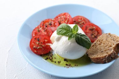 Lezzetli burrata peyniri, domates, fesleğen ve ekmek beyaz masada, yakın plan.