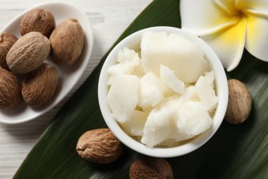 Tabakta Shea yağı, beyaz ahşap masada çiçek ve fındık, düz yatıyordu.