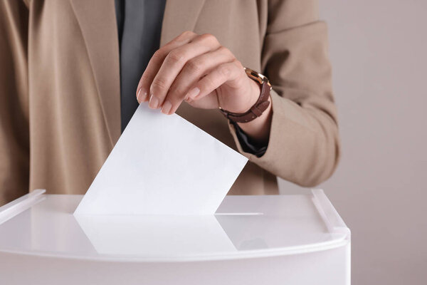 Woman putting her vote into ballot box against grey background, closeup