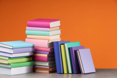 Turuncu arka planda ahşap masadaki renkli kitap yığınları
