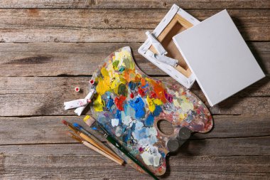 Sanatçı paleti, fırçalar, boyalar ve tahta masa üzerindeki boş tuvaller, düz yatış.