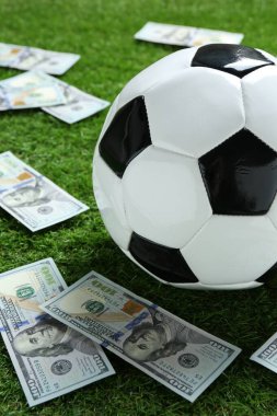 Yeşil çimlerin üzerinde futbol topu ve dolar banknotları, yakın plan.