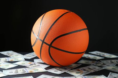 Basketbol topu ve dolar banknotları siyah masada.