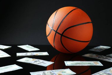 Siyah arka planda basketbol topu ve dolar banknotları