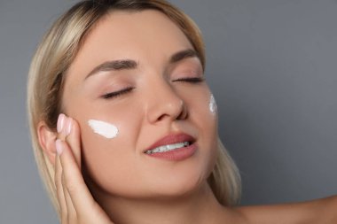 Gri arka planda krem sürmüş güzel bir kadın, yakın plan.