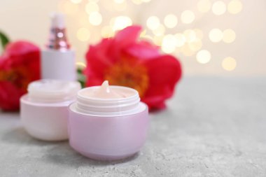 Gri masa üzerinde farklı kozmetik ürünleri ve şakayık çiçekleri var. Arka planda ise bulanık ışıklar var. Yakın plan. Metin için boşluk