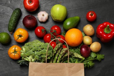 Vejetaryen yemek servisi. Farklı taze sebzelerle dolu kağıt poşet ve koyu dokulu masa üzerinde meyveler, düz uzanmış.