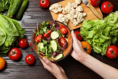 Sağlıklı vejetaryen yemekleri. Sebzeli ahşap masada salata tutan kadın.