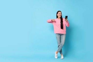 Açık mavi arka planda akıllı telefonu olan gülümseyen bir kadın. Metin için boşluk