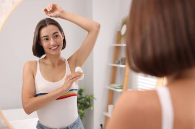 Gülümseyen kadın evde aynanın yanında deodorant sürüyor.