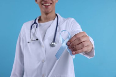 Prostat kanseri farkındalığı. Doktor, açık mavi kurdeleyi renk arkaplanı ve seçici odak üzerine desteğin sembolü olarak tutuyor