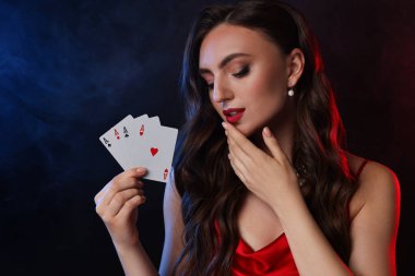 Poker oyunu. Siyah arka planda renkli ışıklar ve dumanla oyun kartları olan büyüleyici bir kadın.