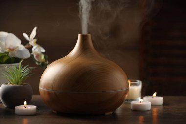 Aroma yağı yayıcı, yanan mumlar ve ahşap masada bitkiler, yakın plan.