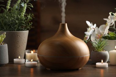 Aroma yağı yayıcı, yanan mumlar ve ahşap masa üzerinde bitkiler.