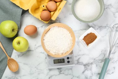 Mutfak terazisinin düz kompozisyonu beyaz mermer masa üzerinde un ve ürünlerle doluydu.