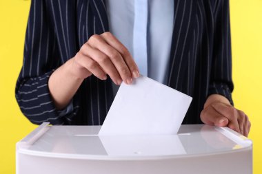 Kadın oyunu sarı arka plana karşı sandığa koyuyor, yakın plan.