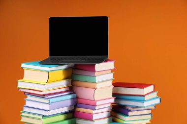 Turuncu arka planda renkli kitap ve dizüstü bilgisayar yığınları