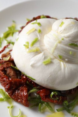Lezzetli burrata peyniri ve tabakta kurutulmuş domatesler, yakın plan.