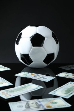 Siyah arka planda futbol topu ve dolar banknotları