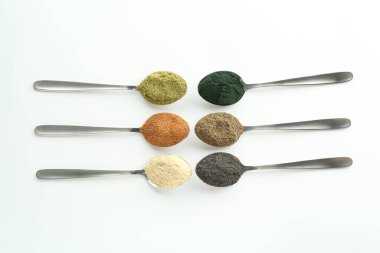 Beyaz arka planda kaşıklarda farklı süper yiyecek tozları, düz bir zemin