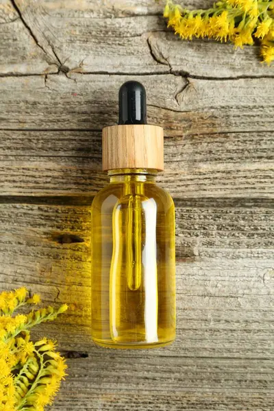 stock image Tincture in bottle and goldenrod flowers on wooden table, top view