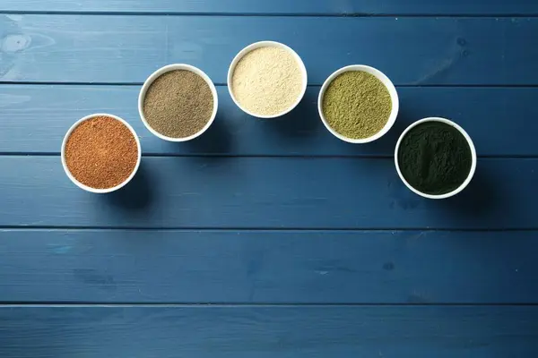 stock image Different superfood powders in bowls on blue wooden table, flat lay. Space for text