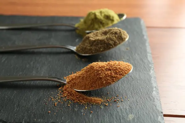 stock image Different superfood powders in spoons on wooden table, closeup