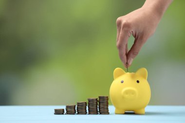 Açık mavi masadaki sarı kumbaraya para koyan kadın arka planda bulanık, yakın plan. Metin için boşluk