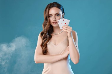 Poker oyunu. Açık mavi arka planda elinde iskambil kağıtları tutan hoş bir kadın.